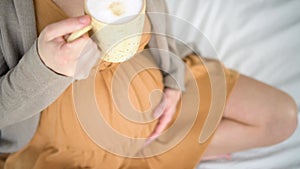 Cute pregnant woman holds in hand a cup of coffee. Concept of a happy pregnancy. Not healthy drinks