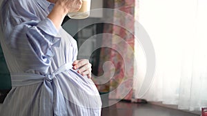 Cute pregnant woman holds in hand a cup of coffee. Concept of a happy pregnancy. Not healthy drinks