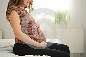 A cute pregnant woman sits in bed. The concept of a happy pregnancy. 9 months of waiting for a baby.