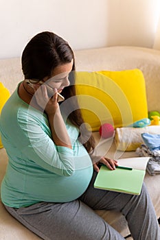 Cute Pregnant Woman writing packing list for maternity hospital With Notebook Prepares bags. Young Ledy In Pregnancy