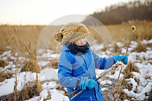 Cute preschool boy is playing on the ice of a frozen lake or river on a cold sunny winter sunset. Child having fun with icicle and