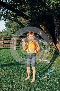Cute preschool Caucasian child boy blowing soap bubbles in park at summer sunset