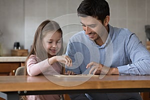 Cute preschool daughter and father play checkers at home