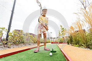 Cute preschool girl playing mini golf with family. Happy child having fun with outdoor activity. Summer sport for