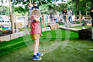 Cute preschool girl playing mini golf with family. Happy toddler child having fun with outdoor activity. Summer sport