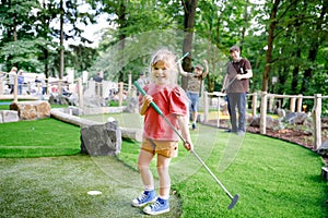 Cute preschool girl playing mini golf with family. Happy toddler child having fun with outdoor activity. Summer sport