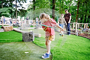 Cute preschool girl playing mini golf with family. Happy toddler child having fun with outdoor activity. Summer sport