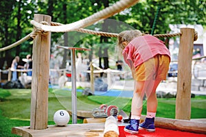 Cute preschool girl playing mini golf with family. Happy toddler child having fun with outdoor activity. Summer sport