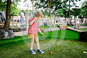 Cute preschool girl playing mini golf with family. Happy toddler child having fun with outdoor activity. Summer sport