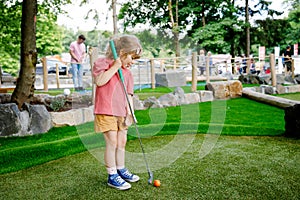 Cute preschool girl playing mini golf with family. Happy toddler child having fun with outdoor activity. Summer sport