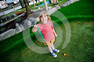 Cute preschool girl playing mini golf with family. Happy toddler child having fun with outdoor activity. Summer sport