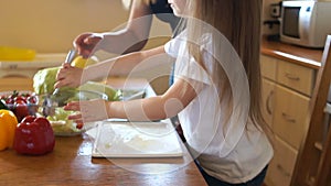 Cute preschool girl spooning salad in the kitchen. Mom`s helper. Daughter and mother are preparing a vegetarian salad