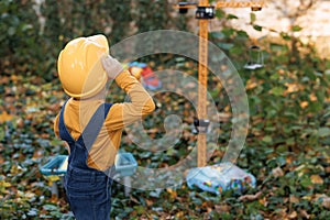 Cute preschool young kid builder boy wearing protective yellow helmet on background construction cranes on site. Future