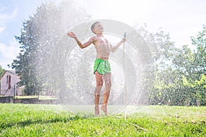 Cute  preschooler boy refresh herself from garden watering hose on the family country house grass yard