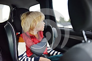 Cute preschooler boy sitting in a car seat and wearing a belt. Ð¡hild is looking out the window of a car during a family trip.