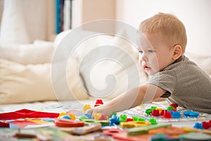 Cute preschooler child boy plays with mosaic at home. A blond little toddler playing in kid`s room. Leisure activities