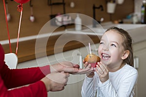 Cute preschooler girl celebrating 6th birthday. Mother giving daughter birthday cupcake with a candle. Childrens birthday party.