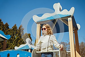 Cute preschooler girl climbing on a playground equipment on the blue sky background. happy girl in beige jacket and