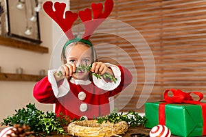 Cute preschooler girl dressed up for xmas making christmas wreath in living room. Christmas decoration family fun concept.