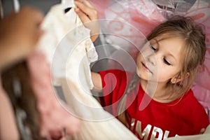 Cute preschooler girl has chosen a new lovely dress among a lot of clothes in child fashion store