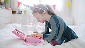 Cute preschooler girl with unicorn hair decoration playing with children cosmetic and applying makeup