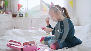 Cute preschooler girl with unicorn hair decoration playing with children cosmetic and applying makeup