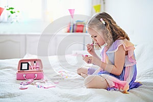 Cute preschooler girl with unicorn hair decoration playing with children cosmetic and applying makeup