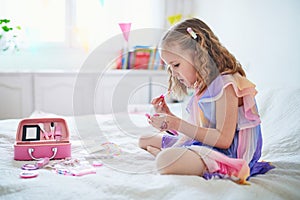 Cute preschooler girl with unicorn hair decoration playing with children cosmetic and applying makeup