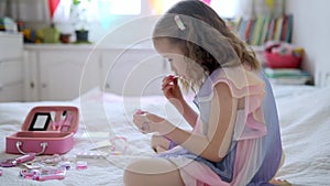 Cute preschooler girl with unicorn hair decoration playing with children cosmetic and applying makeup.