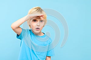 Cute preschooler looking curiously into distance with hand on the forehead. Kid looking into future, studio portrait.