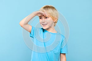 Cute preschooler looking to distance with hand on the forehead, smiling. Kid looking into future, studio portrait. photo