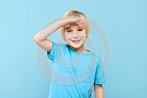 Cute preschooler looking to distance with hand on the forehead, smiling. Kid looking into future, studio portrait.