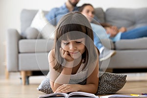 Cute preschooler lying on floor reading interesting book