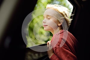 Cute preteen boy inhales the air of freedom from car window during family road trip and enjoy of pleasant expectation of happy