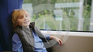 Cute preteen boy is traveling in a local train carriage or by railroad while it rain outside