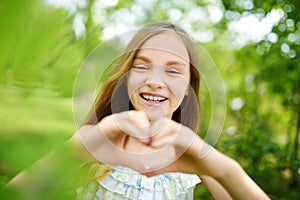Cute preteen girl laughing and holding her hands in a heart shape on bright and sunny summer day. Cute child enjoying herself outd