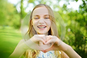Cute preteen girl laughing and holding her hands in a heart shape on bright and sunny summer day. Cute child enjoying herself outd