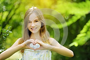 Cute preteen girl laughing and holding her hands in a heart shape on bright and sunny summer day. Cute child enjoying herself outd