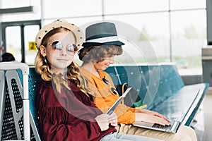 Preteen kids sitting in waiting hall with laptop and passport