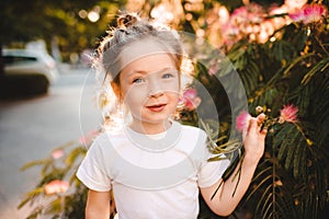 Cute pretty child 4-5 year old smell flowers in city street outdoor over nature background close up.