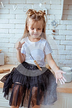 Cute pretty little caucasian girl with long hair in white t-shirt and black skirt cooking in the kitchen