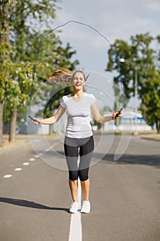 Cute and pretty young girl exercising with a jumping rope on a park background. Gymnastics concept.