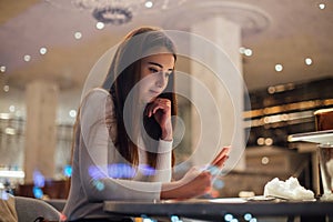 Cute and pretty young woman on smartphone in cafe