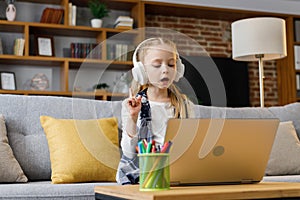 Cute primary school girl studying at home using laptop computer. Serious child doing homework, answering online test