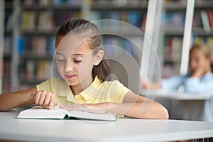 Cute pupil perusing a book at the library desk