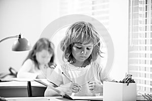 Cute pupil writing at desk in classroom at the elementary school. Student boy doing test in primary school. Children