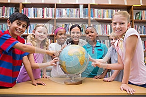 Cute pupils and teacher looking at globe in library