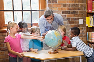 Cute pupils and teacher looking at globe in library