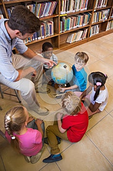 Cute pupils and teacher looking at globe in library