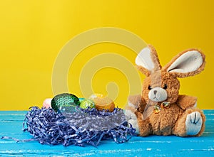 Cute rabbit toy and decorative Easter eggs with sequins on a yellow background